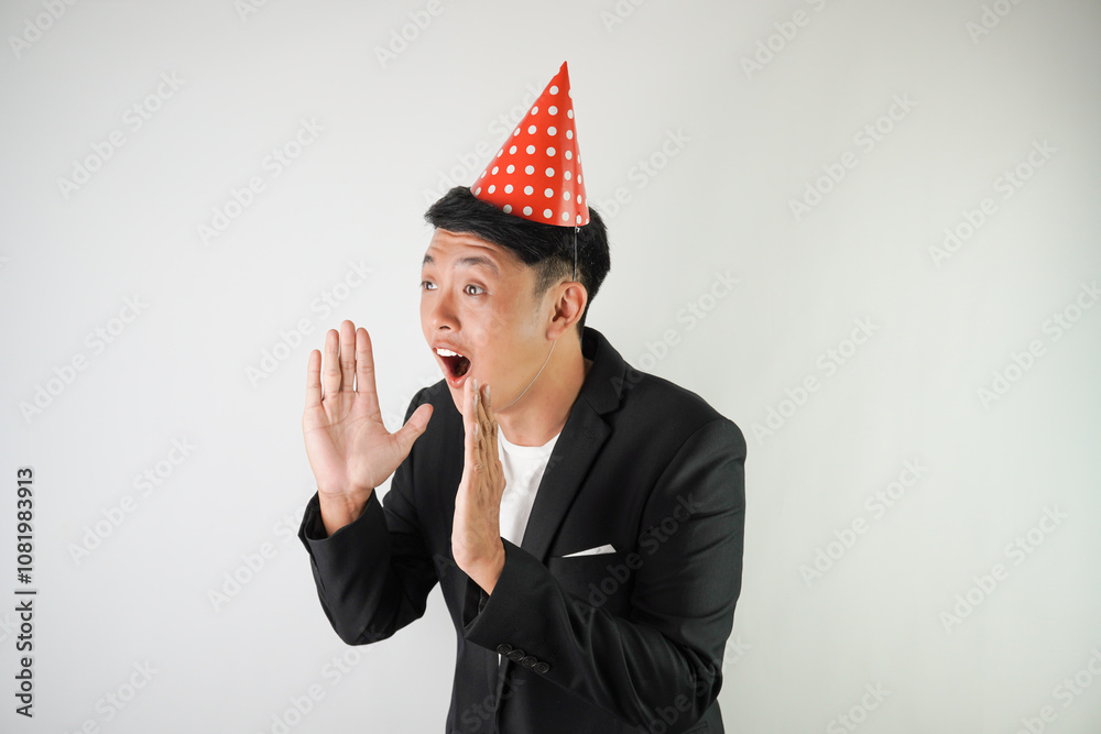 Excited young asian man wearing red party hat, white shirt and black suit is shouting to the audience people, isolated over white background. Concept for Christmas Holiday and New Year Party Excited young asian man wearing red party hat, white shirt and black suit is shouting to the audience people, isolated over white background. Concept for Christmas Holiday and New Year Party