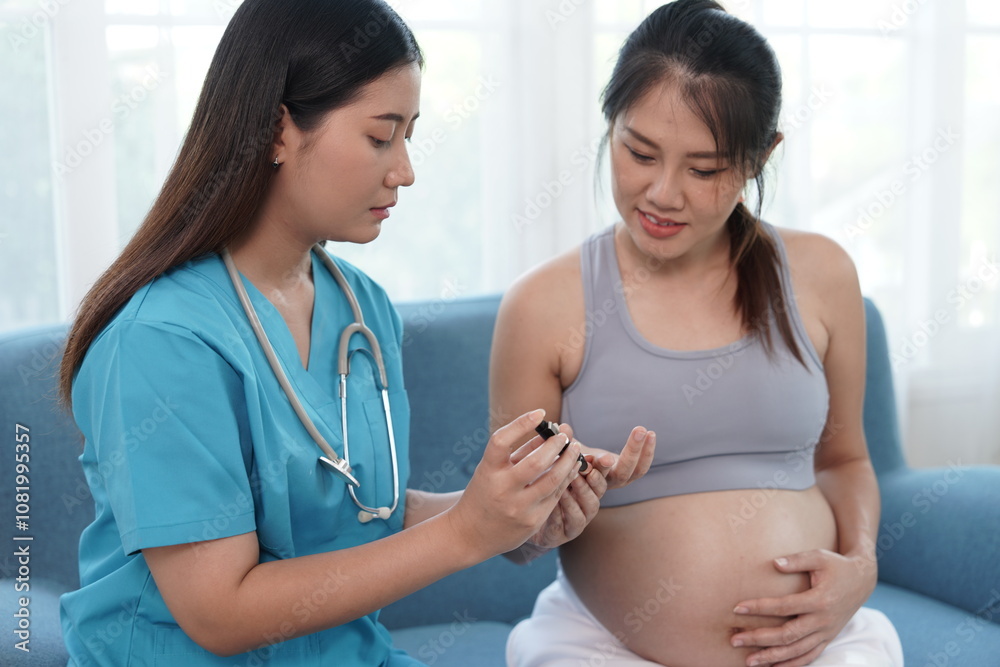 Asian nurse uses a needle to prick fingertip to test blood sugar level of a seven-month pregnant Asian woman in sports bra sitting on the couch at home.