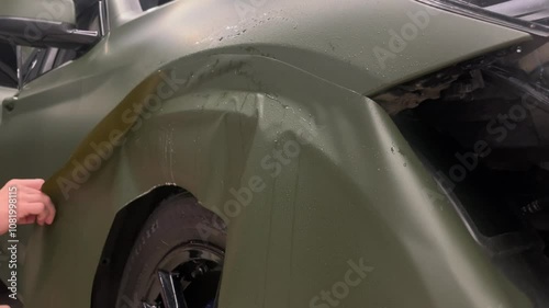 A specialist in wrapping a car with green khaki vinyl or ppf film in the process of work. Car wrapping specialists cover the car with green vinyl film. Khaki green vinyl foil. Selective focus.