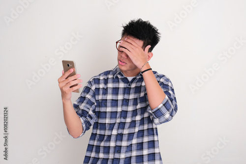 Young Asian man showing regret gesture when staring at his mobile phone photo