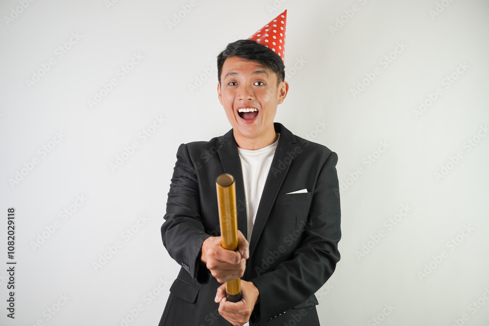 Excited young asian man wearing red party hat, white shirt and black suit is holding confetti cannon, isolated over white background. Concept for Christmas Holiday and New Year Party Excited young asian man wearing red party hat, white shirt and black suit is holding confetti cannon, isolated over white background. Concept for Christmas Holiday and New Year Party