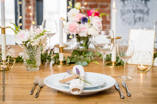 An elegant table setting with white plates, a lavender-tied napkin, crystal glassware, and gold candle holders. Floral arrangements with pastel blooms and candles add warmth to this sophisticated tabl