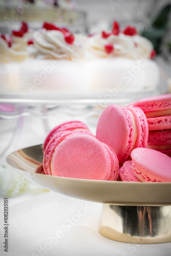 A close-up of pink macarons on a golden plate, with a blurred dessert backdrop. The vibrant color and refined presentation make these macarons perfect for a luxurious dessert display. photo