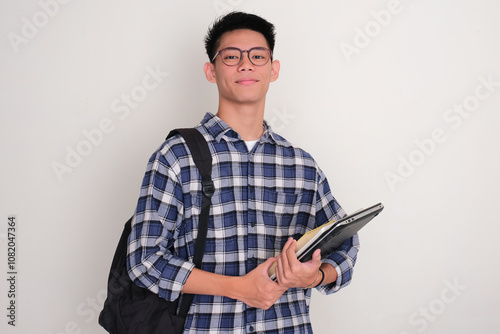 Indonesian college student smiling confident while holding books, laptop and carrying backpack photo