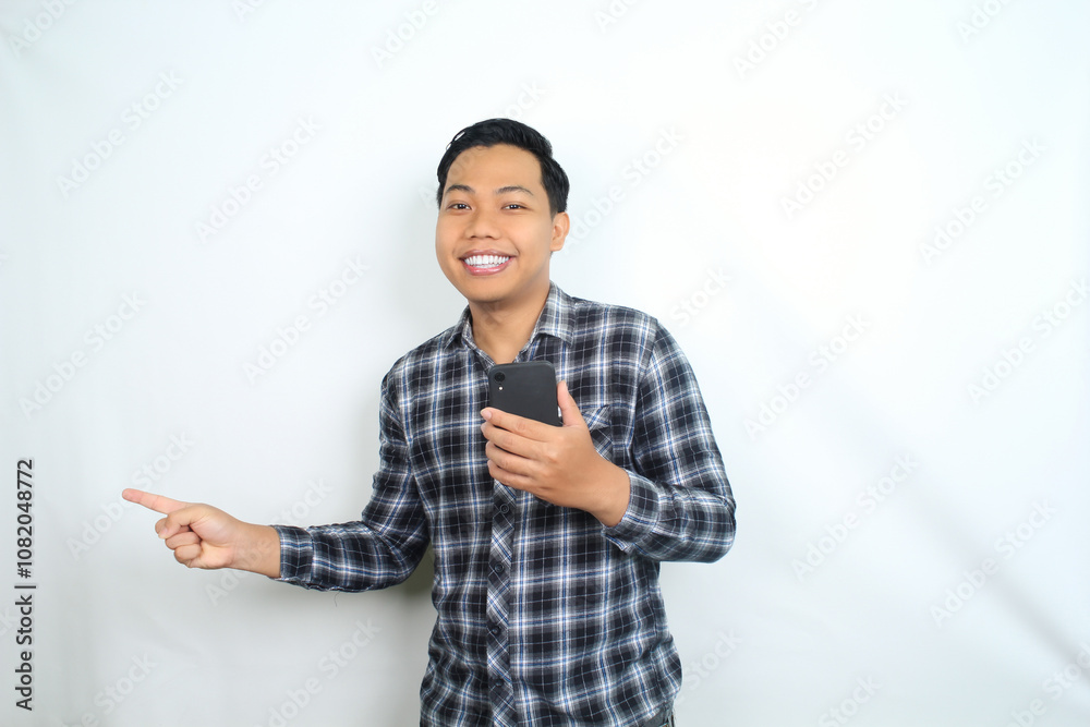 smiling asian man pointing to copy space with holding mobile phone isolated on white background smiling asian man pointing to copy space with holding mobile phone isolated on white background