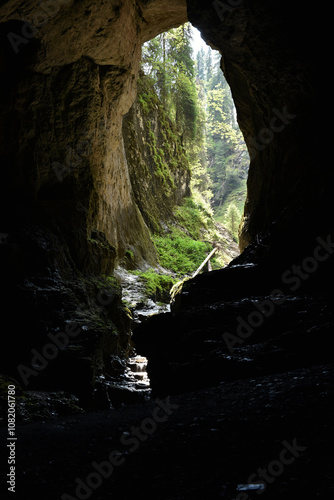 Silhouette of a big cave entrance from inside, water stream flowing into cave