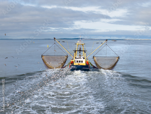 Foto Aerial of fishing ship, boat trawling nets with gulls at Wadden sea