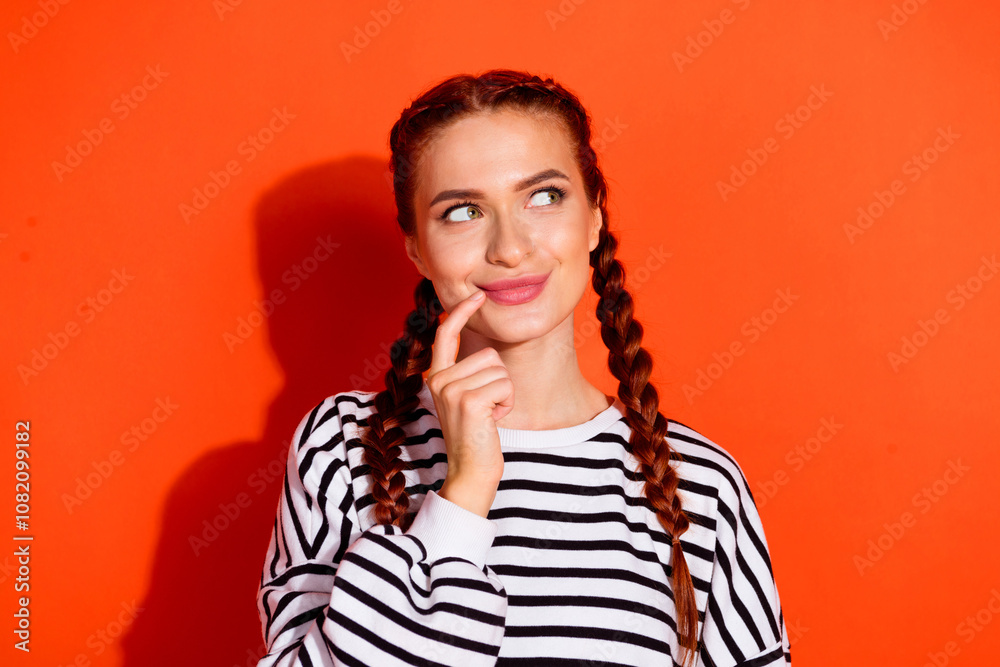 Fototapeta premium Charming young woman in striped pullover with playful expression against vibrant orange background