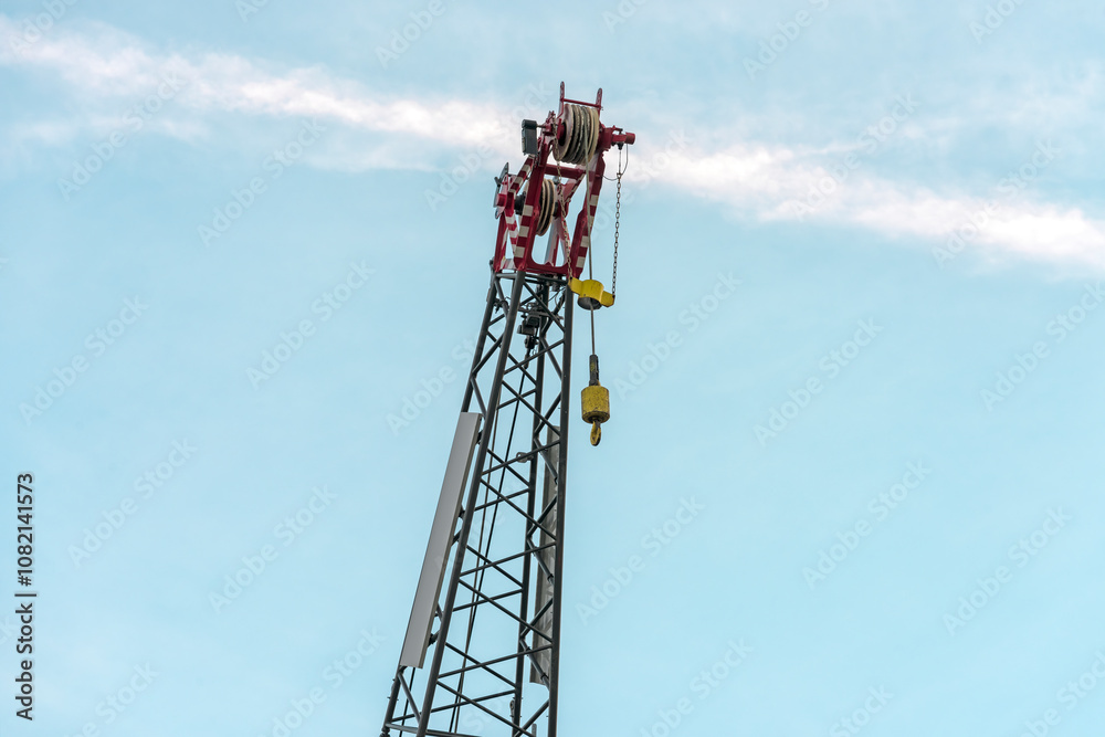 industrial crane with lifting hook stands out against a light blue sky