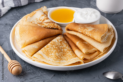 Stack of traditional russian pancakes blini with honey and sour creamon gray background