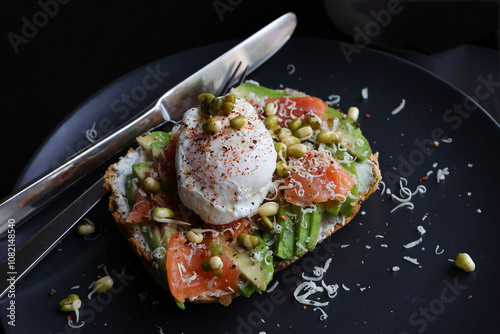 Poached eggs on top of smashed avocado on sourdough toast with smoked salmon and mung bean sprouts. Healthy breakfast with plate on table. Angel view. Copy space left
