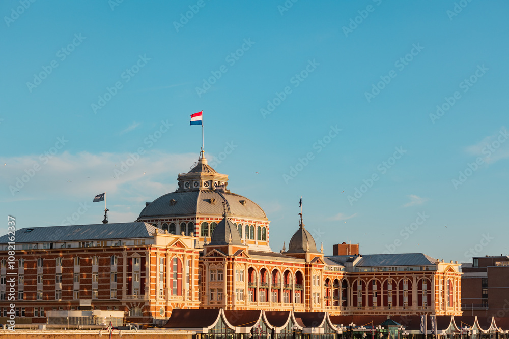 Naklejka premium Kurhaus in Scheveningen during sunset. The Dutch flag on top of the building.