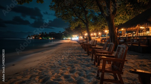 A row of chairs on a sandy beach at night with the ocean in the background.