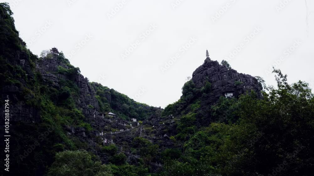 low angle shot of Hang Múa Viewpoint in Ninh Binh, Vietnam, from the bottom. dramatic valley framed by rocky cliffs, winding stone stairs leading to the summit, hilltop pagoda and tower Tam Coc low angle shot of Hang Múa Viewpoint in Ninh Binh, Vietnam, from the bottom. dramatic valley framed by rocky cliffs, winding stone stairs leading to the summit, hilltop pagoda and tower Tam Coc
