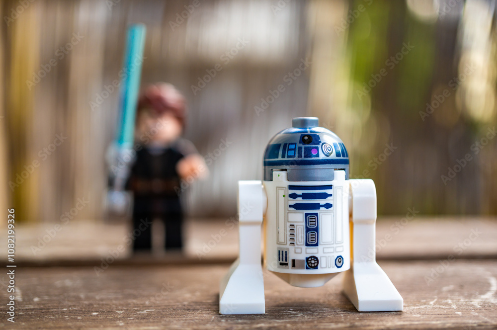 Obraz premium Lego Star Wars R2 D2 toy robot on the foreground and a Skywalker with blue laser sword