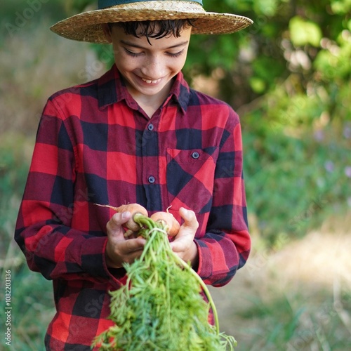 boy in straw hat and checkered shirt with a bunch of carrots picked in the garden photo