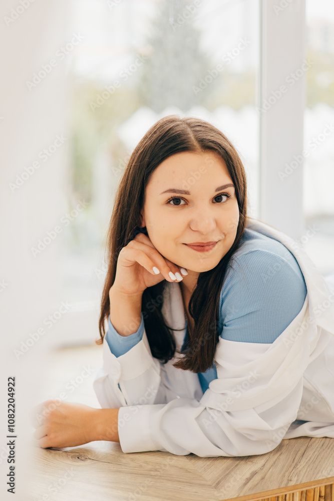 girl lying on her stomach on the windowsill, pensive look, slight smile in a white shirt and light jeans girl lying on her stomach on the windowsill, pensive look, slight smile in a white shirt and light jeans