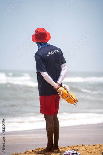 Indian lifeguard in red cap and blue shirt looking out into the ocean keeping watch for swimmers in danger in Goa photo