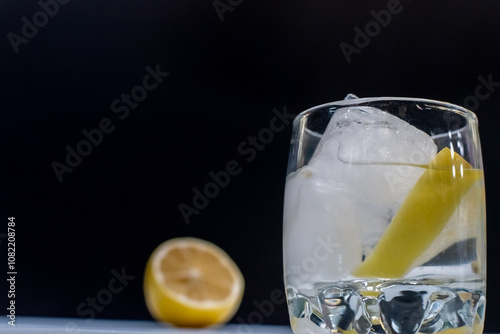 Glass with vodka, lemon and ice close-up on dark deep background