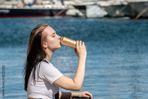 Young woman drinking beer from a can on the embankment with yachts,boats on the sea