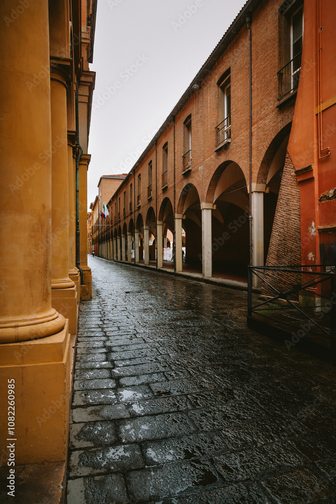 Fototapeta premium Wet stone pavement reflecting arcades of historical buildings in bologna, italy, creating a picturesque scene after the rain