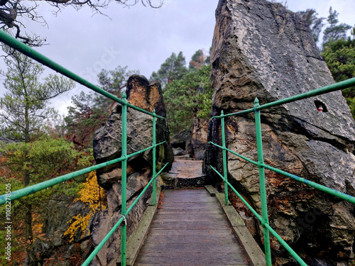 hikers walk along a narrow ridge high above autumn woods and meadows. walkways and bridges leading between rock outcrops photo