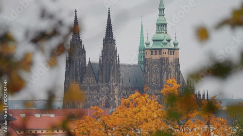 The Gothic spires and green dome of St. Vitus Cathedral rise against a clear sky, showcasing Prague’s heritage. Vibrant autumn vegetation in the foreground. photo