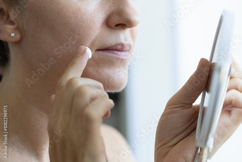 Woman in front of the mirror applying anti agin cream on wrinkles on her face. Closeup, selective focus.