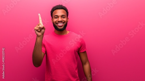 A cheerful young man in a pink shirt poses against a vibrant pink background, raising his index finger to signal an important point