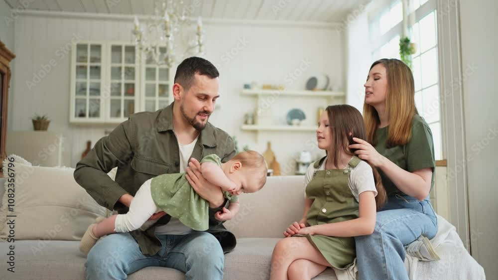 Happy family at home. Mother father two children daughters relaxing on sofa indoor. Mom dad parents baby girls kids relax playing having fun together. Family smiling laughing enjoying tender moment Happy family at home. Mother father two children daughters relaxing on sofa indoor. Mom dad parents baby girls kids relax playing having fun together. Family smiling laughing enjoying tender moment