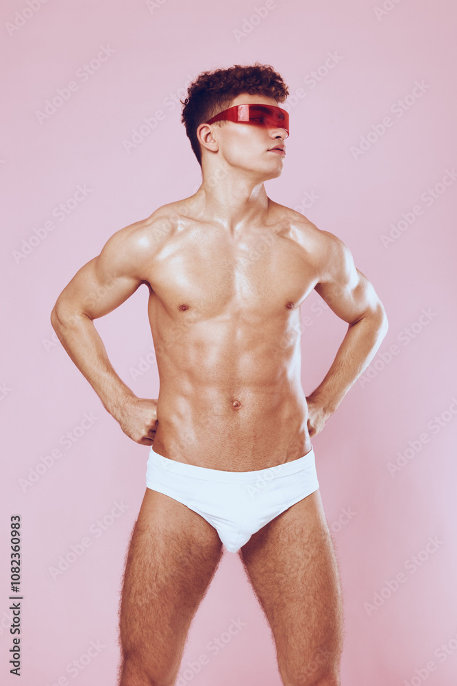 Fototapeta premium Confident young man posing in stylish sunglasses and white swimwear against a pink background, showcasing his toned physique. Fashion and lifestyle concept.