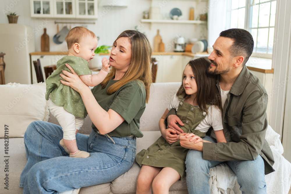 Happy family at home. Mother father two children daughters relaxing on sofa indoor. Mom dad parents baby girls kids relax playing having fun together. Family smiling laughing enjoying tender moment Happy family at home. Mother father two children daughters relaxing on sofa indoor. Mom dad parents baby girls kids relax playing having fun together. Family smiling laughing enjoying tender moment
