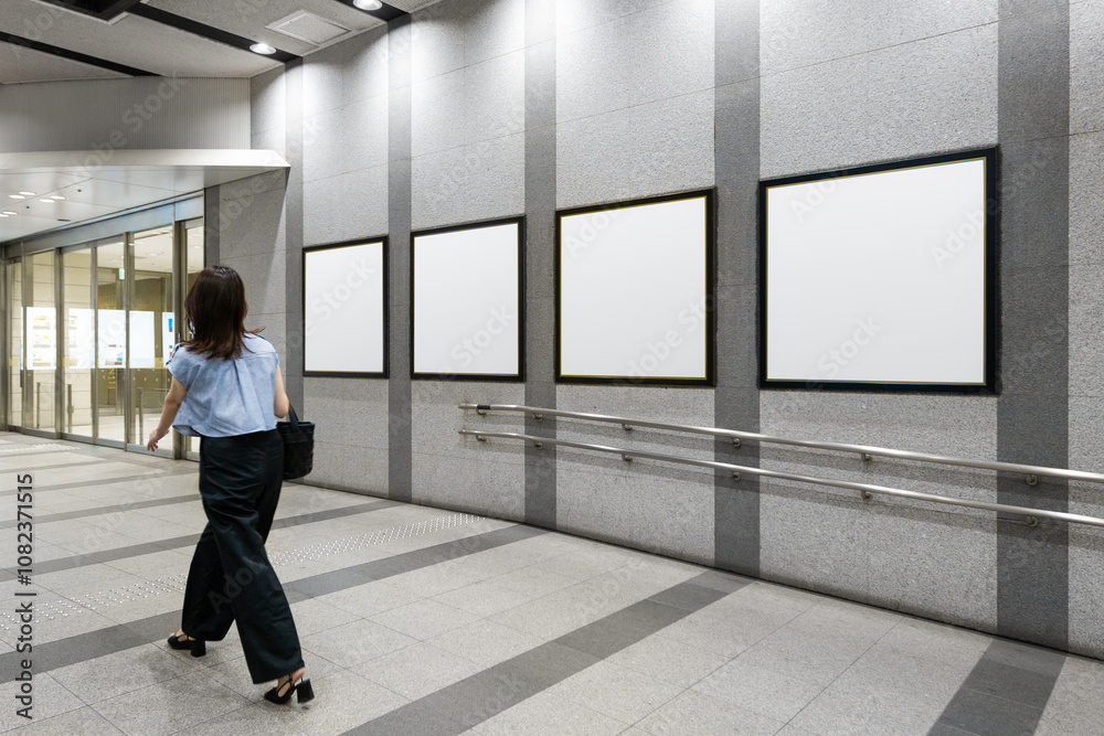 An executive japanese woman walks past four blank billboard advertising posters on a subway station hall. There is space for text for advertising signage ideas for a mockup