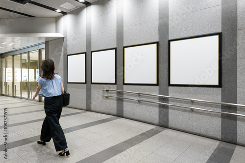 Obraz na płótnie An executive japanese woman walks past four blank billboard advertising posters on a subway station hall. There is space for text for advertising signage ideas for a mockup w salonie