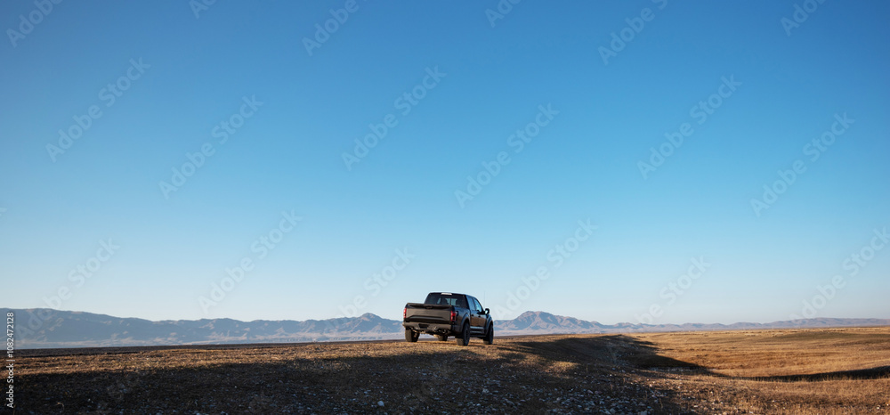 Fototapeta premium the freedom of exploration, with a solitary vehicle paused on a vast, open landscape, dwarfed by the vastness of the sky and distant mountains on the horizon.