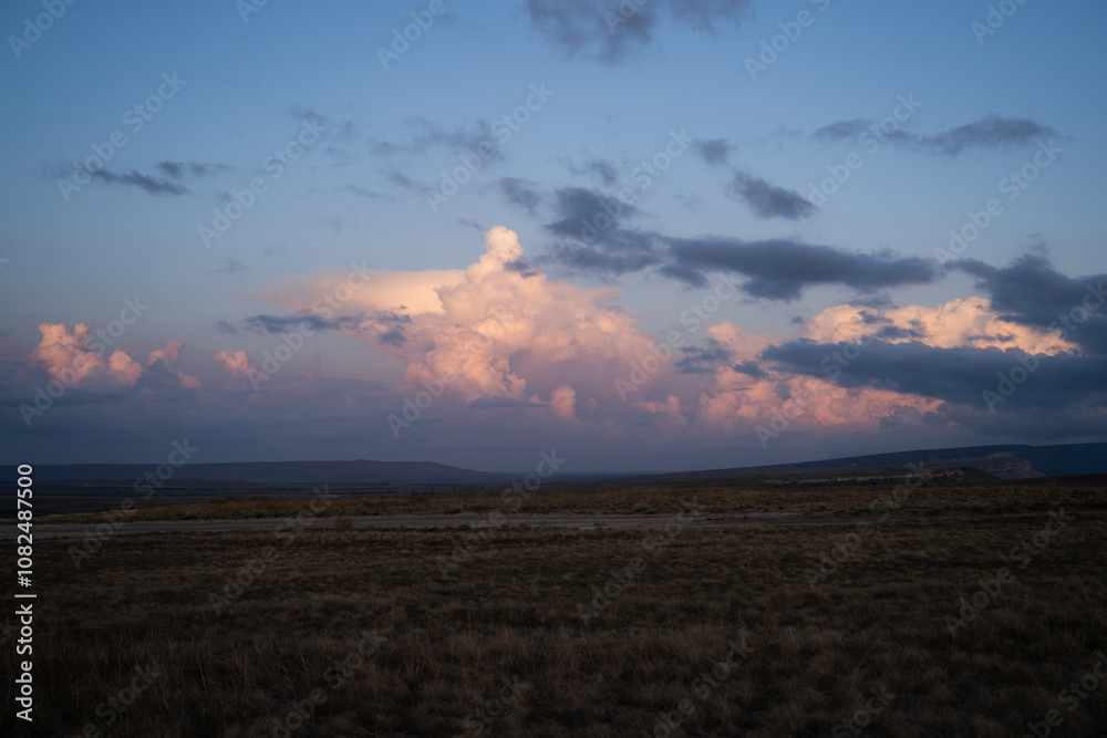 Obraz premium View of a sunset over a field of grass, a beautiful sunset with a purple, pink, and blue as the sun dips below the horizon, dramatic sky at dusk or dawn with fluffy cumulus clouds, mood setting image