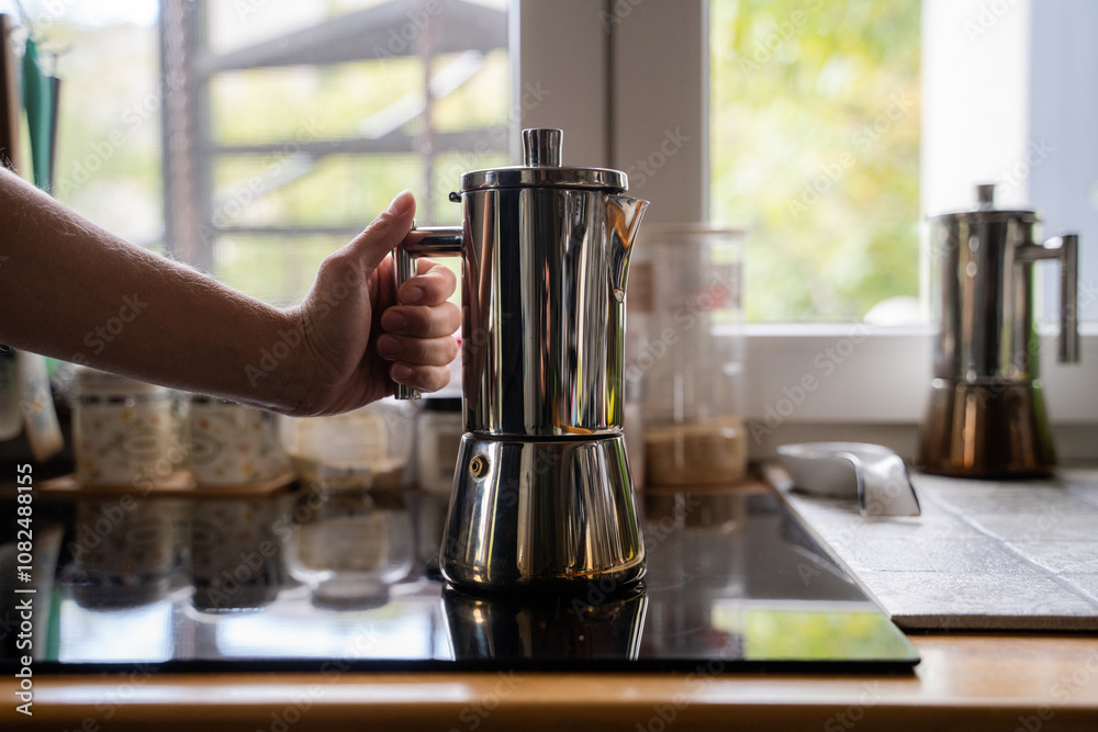 Woman preparing coffee at home kitchen setting near window, girl holding a modern stainless geyser coffee pot on induction stove panel indoor, geyser coffee maker