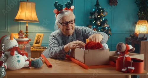 Happy old 90s grandmother preparing Christmas packages at home, putting crocheted stuffed toys into cardboard boxes packing holiday gifts for children and grandchildren