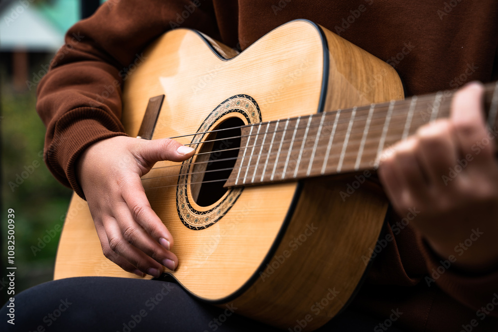 Fototapeta premium Young woman playing acoustic guitar outdoor, close up of teenage girl plays guitar, sitting relaxing and unwinding on weekend, leisure, music, hobby, lifestyle concept, happy guitarist