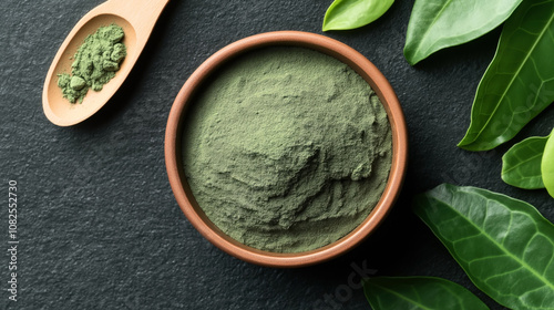 Green matcha tea powder in a wooden bowl with a spoon and fresh green leaves on a dark stone surface
