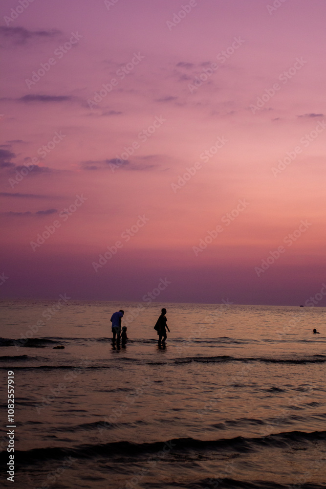 Fototapeta premium a sunset with people standing in the water and one is wearing a pink and orange sunset