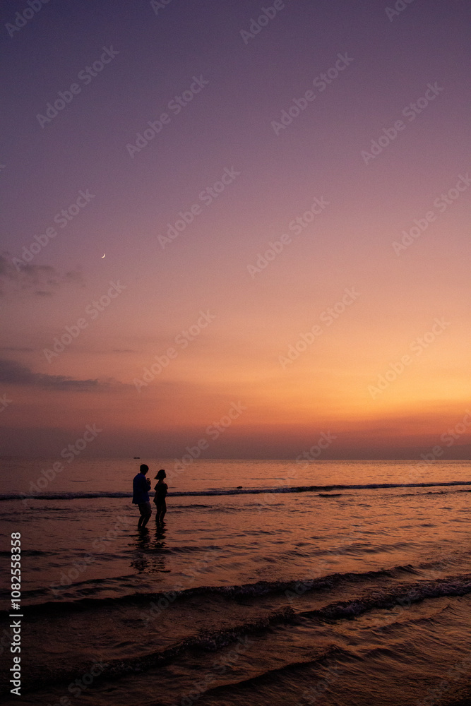 Obraz premium a sunset with people standing in the water and one is wearing a pink and orange sunset