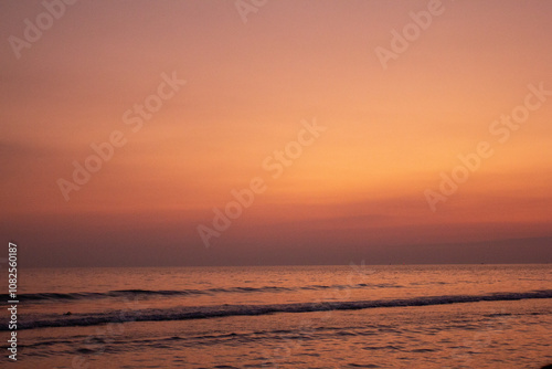 a sunset with people standing in the water and one is wearing a pink and orange sunset