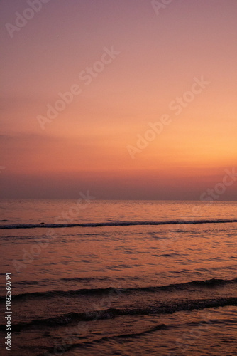 a sunset with people standing in the water and one is wearing a pink and orange sunset
