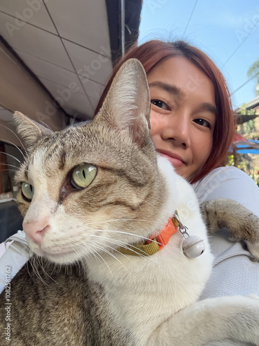 Vertical photo of Thai asian woman holding and taking selfie with her cat, pet lover, good friend.