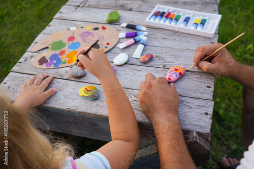 Fototapeta Naklejka Na Ścianę i Meble -  Children education and home school concept. Dad and daughter paint with acrylic paints on sea rocks