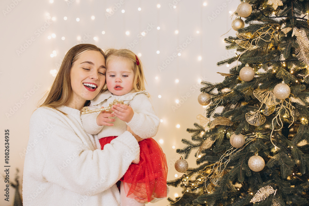Mother and daughter decorating christmas tree with golden ornaments Mother and daughter decorating christmas tree with golden ornaments