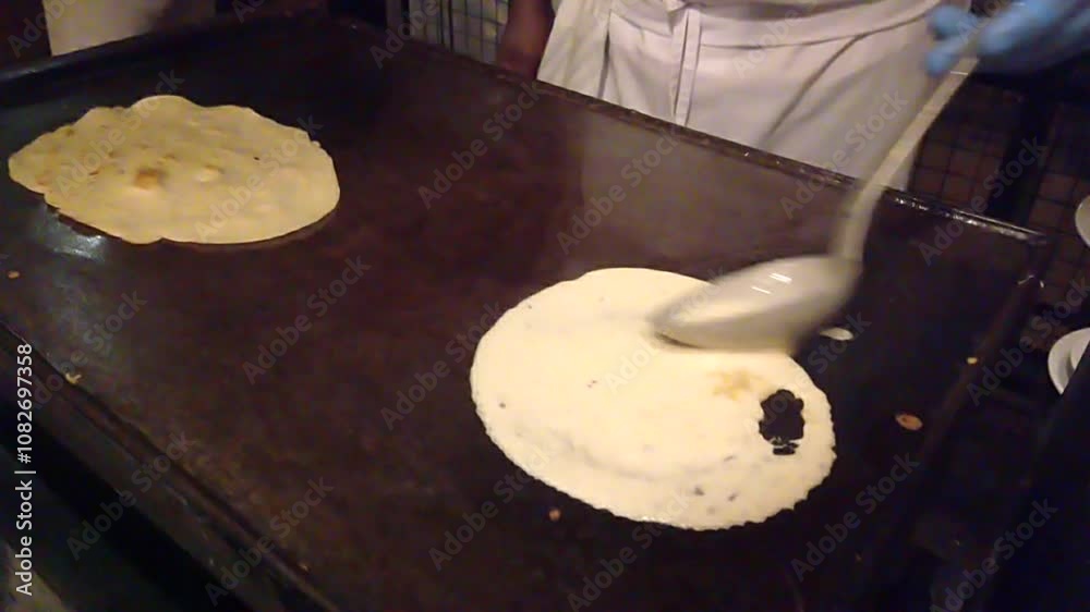 Chef pours batter onto a hot griddle in a restaurant kitchen, creating a thin pancake like food