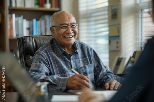 Retirement Planning and Financial LiteracyA smiling elderly man in a patterned shirt sits at a desk, engaged in conversation with someone off-camera, showcasing a warm and inviting atmosphere.