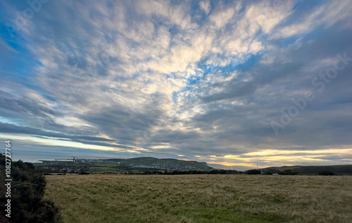 View over fields and coast to Port Erin, Isle of Man. View of town, sea and beach with coast path in foreground. Hills to rear of the town with cultivated fields. Blue moody clouds and sky. photo